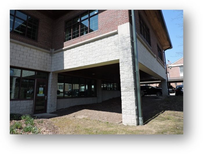A modern building with a brick and stone exterior, featuring large windows and a covered parking area underneath.