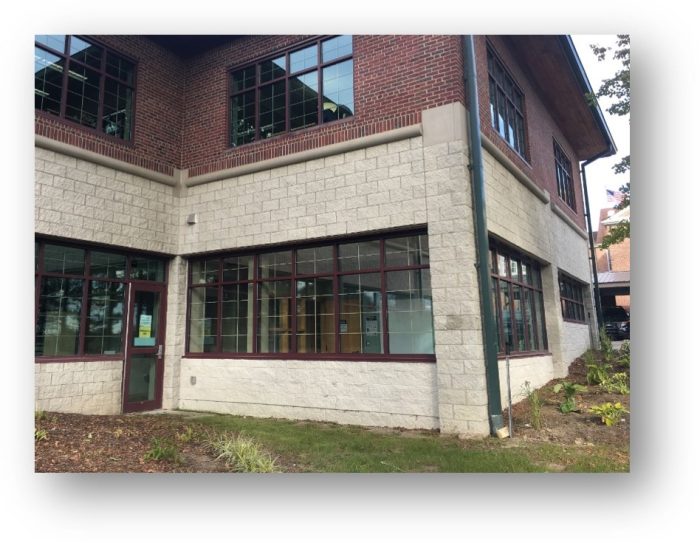 A corner view of a building featuring brick and stone walls, large windows, and a landscaped area in front.